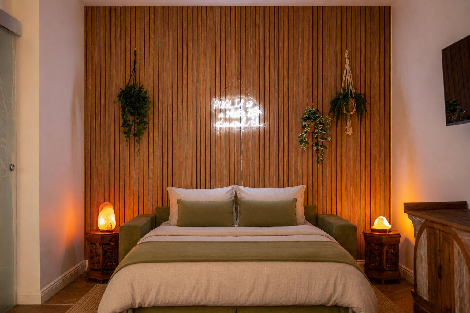 Una camera da letto con parete in listelli di legno, un letto con biancheria verde, due lampade da comodino e piante pensili.