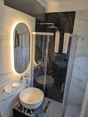 A modern bathroom with a glass-enclosed shower, a round sink, and a mirror with an oval frame. - Private Suite Facing Bari Centrale Station: Elegant and Meticulously Designed Down to the Last Detail (Bari)
