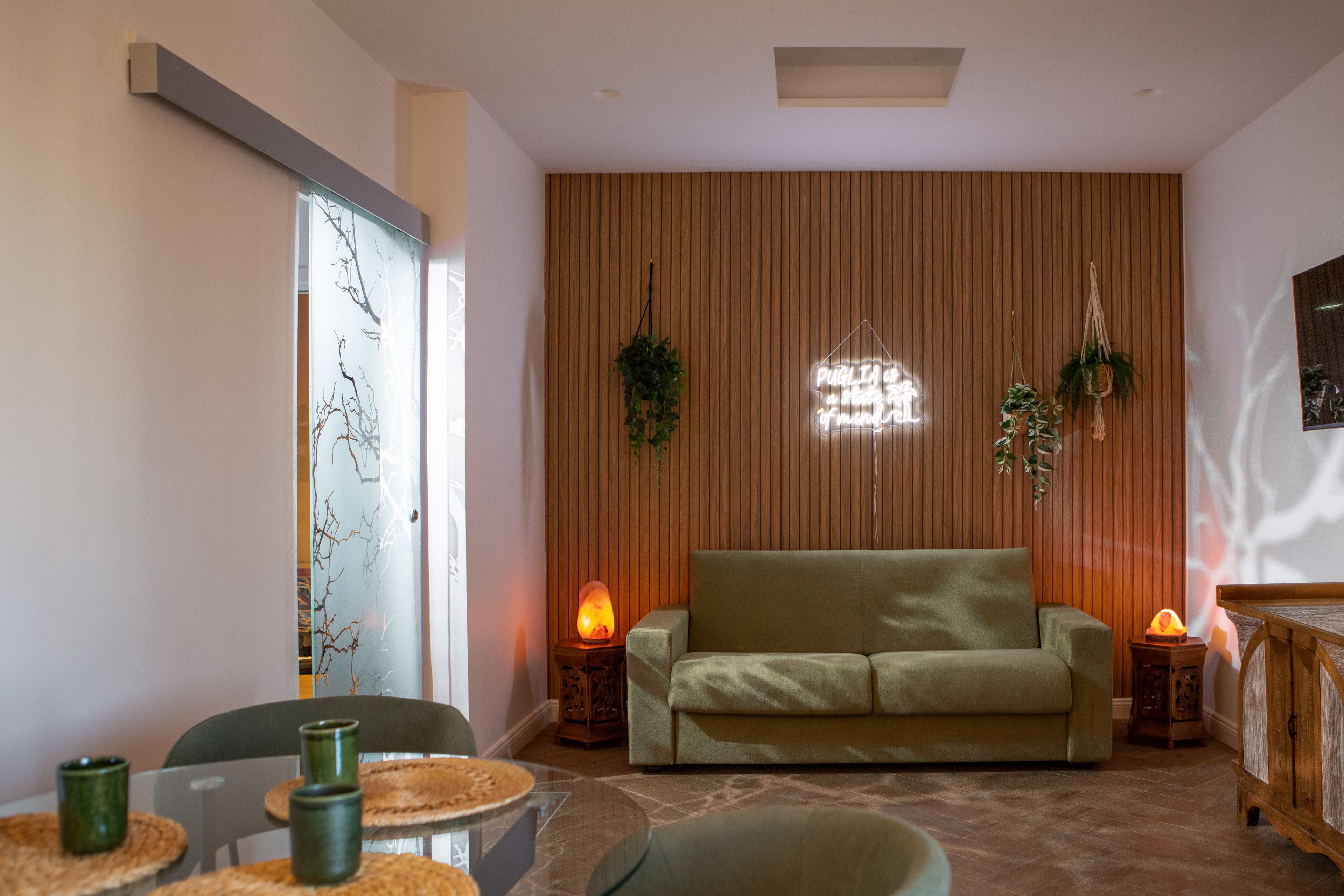 Ein modernes Wohnzimmer mit einer Couch, zwei Beistelltischen mit Lampen, einer Holzwandverkleidung und einer Glastür mit Blick.