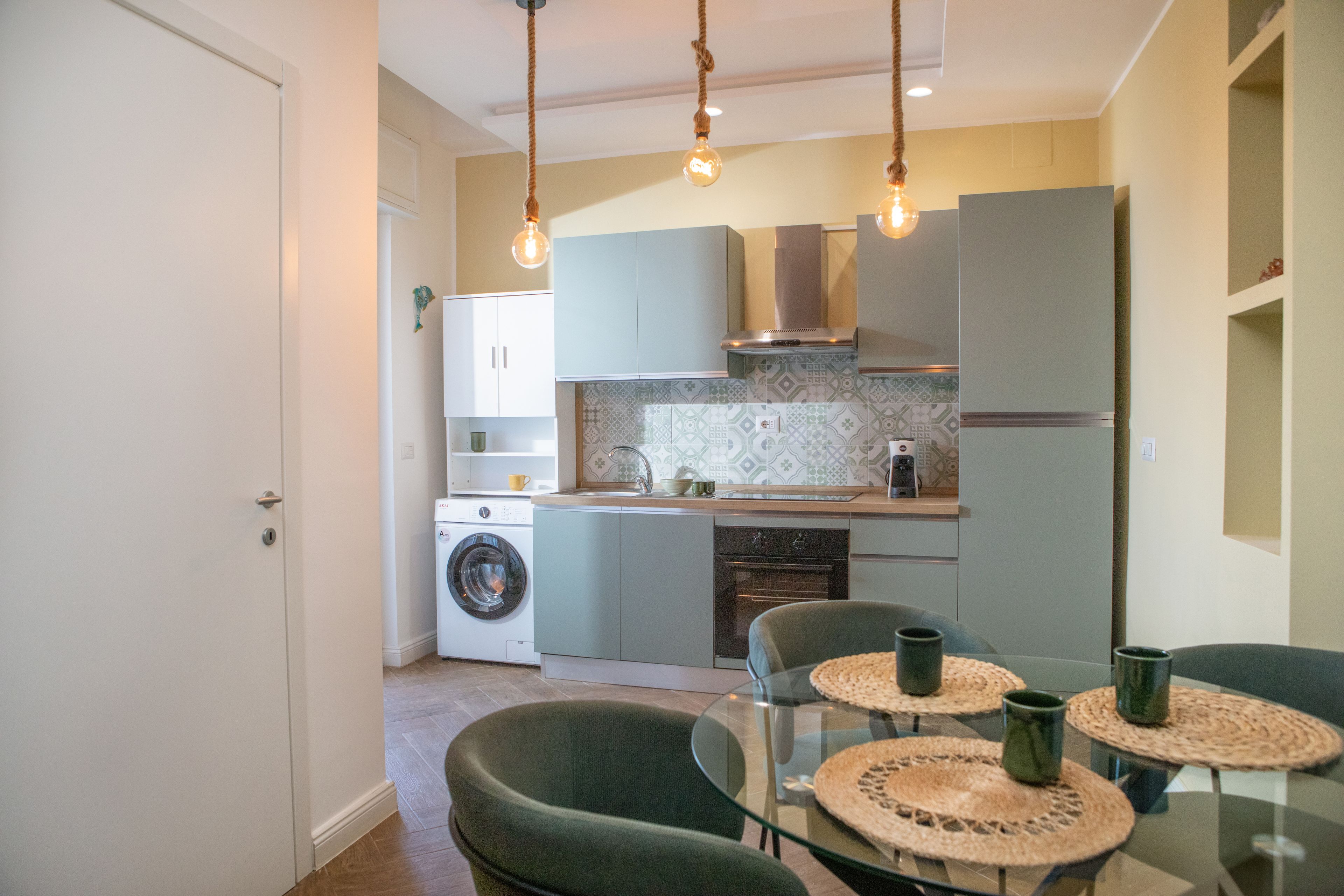 Una cucina compatta con lavatrice, forno integrato e zona pranzo con tavolo e sedie in vetro.