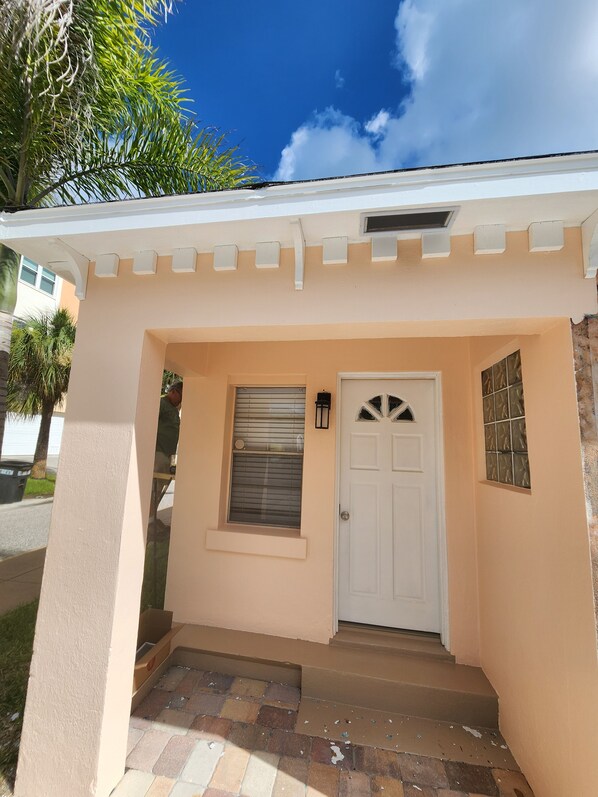 A building entrance with a white door, a window with blinds, and a small porch area.