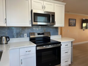 A modern kitchen with white cabinetry, a stainless steel microwave, a black oven, and a marble countertop. - Beautiful 2-bedroom Cottage across the street from the beach. (Indian Shores)