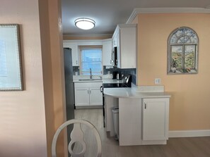 A modern kitchen with white cabinets, a built-in oven, and a window with blinds.