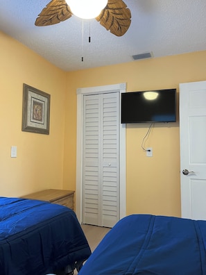 A room with two beds, a ceiling fan, a television mounted on the wall, and a door.