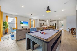 A modern living room with a pool table, a sofa, and a dining area. - 10BR near Disney, sleeps 28, pool, spa & theater (Kissimmee)