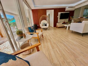 Uma sala de estar moderna com sofá, poltronas, televisão e vista através de amplas janelas.