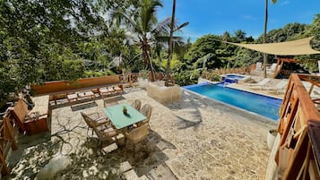 Ein Poolbereich mit Liegestühlen und einem Tisch, umgeben von Palmen und sandigem Untergrund.