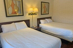 Ein Hotelzimmer mit zwei Betten, einem Nachttisch mit Lampe und Bildern an der Wand.