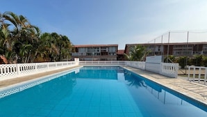 A rectangular swimming pool with a tiled edge, surrounded by a white fence and palm trees. - Ap p/ família, 3 quartos, 5min da praia (Ubatuba)