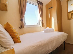 A hotel room with a bed, a window with curtains, a wooden wardrobe, and a mirror. - Sennen Sunset (Penzance)