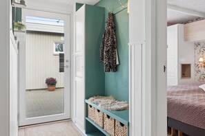 A hallway with a door leading to a balcony, a teal-colored storage unit with baskets, and a bed with a patterned bedspread. - Charming Holiday Home by Ringkøbing Fjord (Skjern)
