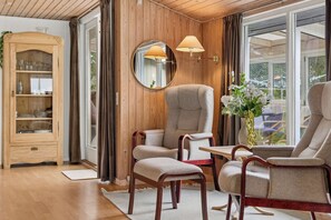 A room with a wooden cabinet, two armchairs, a table, and a mirror. - Charming Holiday Home by Ringkøbing Fjord (Skjern)