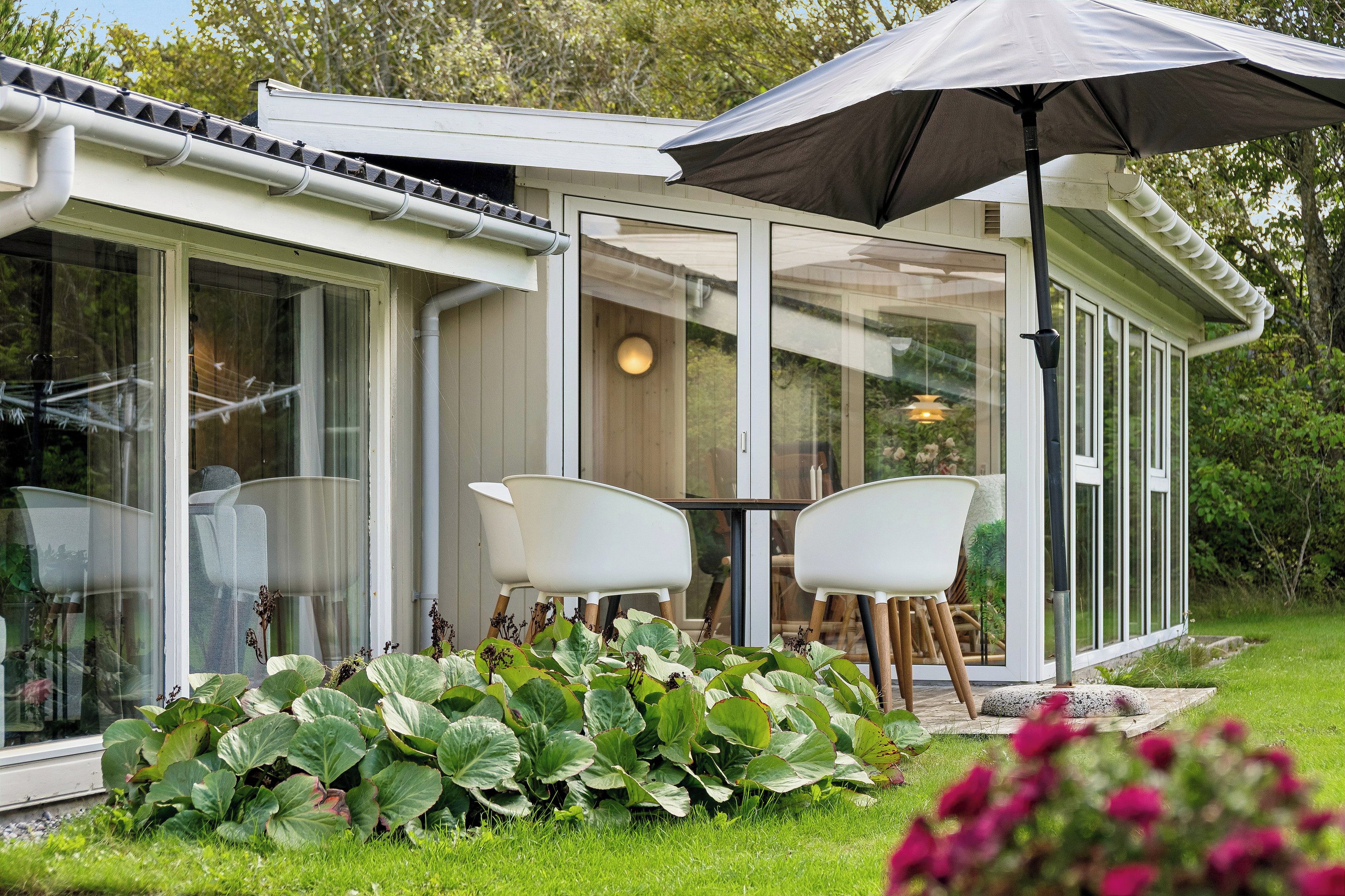 A modern house with a glass conservatory, white furniture, and a garden with large leafy plants.