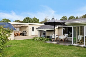 Ein Wohnhaus mit Terrasse, Sitzgelegenheiten im Freien, Grillplatz und überdachtem Außenbereich.