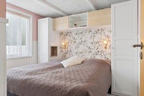 Ein Schlafzimmer mit einem Bett, einem Kleiderschrank, einer Ablage mit Dekoration und einer Wand mit Blumenmuster-Tapete.