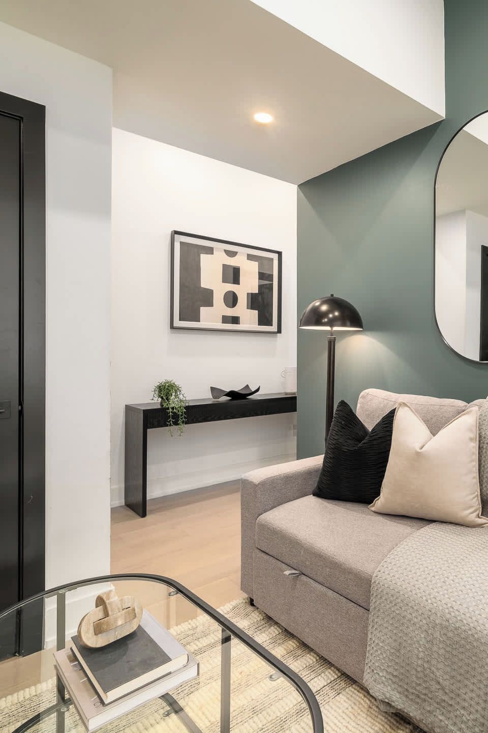 A modern living room with a sofa, a glass coffee table, a black floor lamp, a framed artwork on the wall, and a minimalist console table.