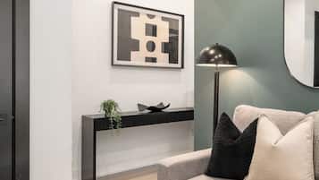 A modern living room with a sofa, a glass coffee table, a black floor lamp, a framed artwork on the wall, and a minimalist console table.