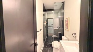 Un baño moderno con cabina de ducha de vidrio, un lavamanos blanco y un inodoro.