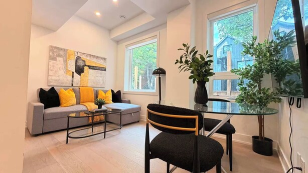 A modern living room with a grey sofa, black and yellow cushions, a glass coffee table, and a black chair with a gold frame.