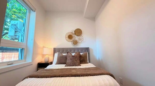 A bedroom with a bed, a nightstand, a lamp, and a decorative wall piece.