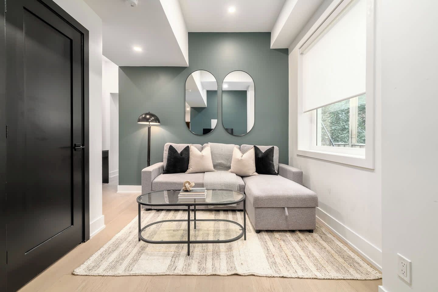 A modern living room with a grey sofa, a glass coffee table, and a large mirror on the wall.