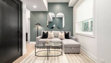 A modern living room with a grey sofa, a glass coffee table, and a large mirror on the wall.