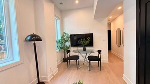 A modern living room with a flat-screen TV, a glass-top dining table, and black chairs.