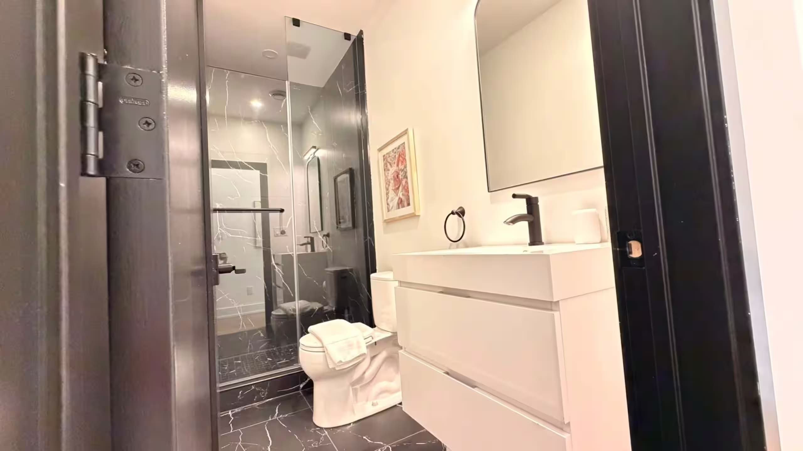 A modern bathroom with a glass shower enclosure, a white toilet, and a vanity with a mirror and sink.