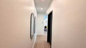 A hallway with a light-colored wall, a door on the right, and a mirror on the left.