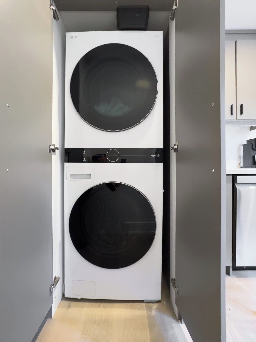 A compact laundry room with two stacked washing machines, a control panel, and a small cabinet.