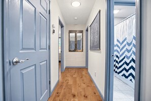 A hallway with wooden flooring, a blue door, a mirror, and a patterned curtain. - Modern Farmhouse w Game Room Near Asheville! (Fairview)