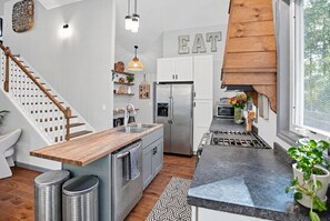 A modern kitchen with a wooden island, stainless steel appliances, and a 'EAT' sign on the wall. - Modern Farmhouse w Game Room Near Asheville! (Fairview)