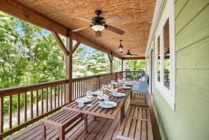An outdoor wooden deck with tables set for dining, a ceiling fan, and a view of trees. - Modern Farmhouse w Game Room Near Asheville! (Fairview)