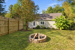 A backyard with a wooden deck, a fire pit, a house, and a large tree. - Modern Farmhouse w Game Room Near Asheville! (Fairview)
