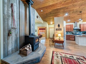 A cozy living room with a wood-burning stove, a dining area with a table and chairs, and a kitchen with wooden cabinets and a tiled backsplash. - Cozy Donnelly Retreat Near Boulder Creek | Wood Stove & Garage (Donnelly)