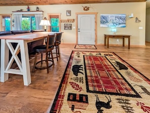 A spacious room with a wooden dining table, chairs, a rug with animal prints, a door, and a painting on the wall. - Cozy Donnelly Retreat Near Boulder Creek | Wood Stove & Garage (Donnelly)