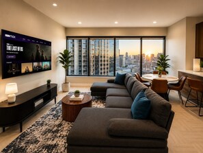 Ein modernes Wohnzimmer mit großem Flachbildfernseher, einer Eckcouch, einem Essbereich und Blick auf die Stadt.