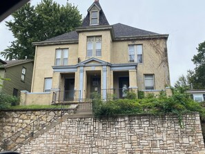 A two-story house with a stone staircase leading to the entrance, a front porch, and a small garden area.