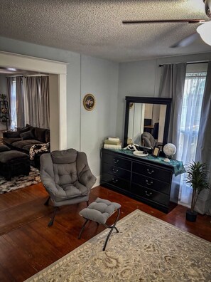 A living room with a dark armchair, a black dresser, a mirror, and a patterned rug.