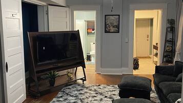 A living room with a television on a stand, a ceiling fan, and a fluffy rug.