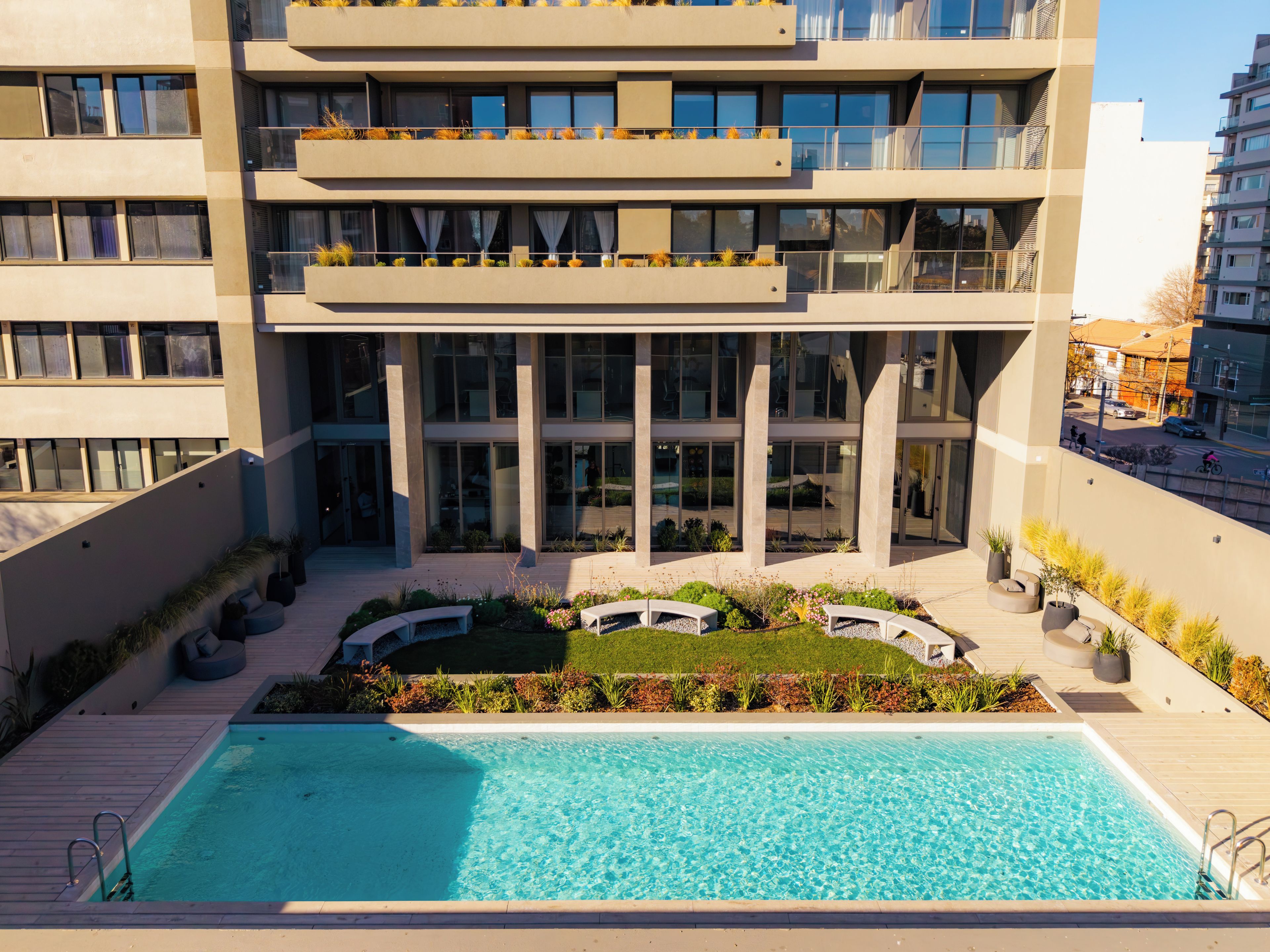 Un edificio moderno con piscina en la azotea, mobiliario exterior y un jardín ajardinado.
