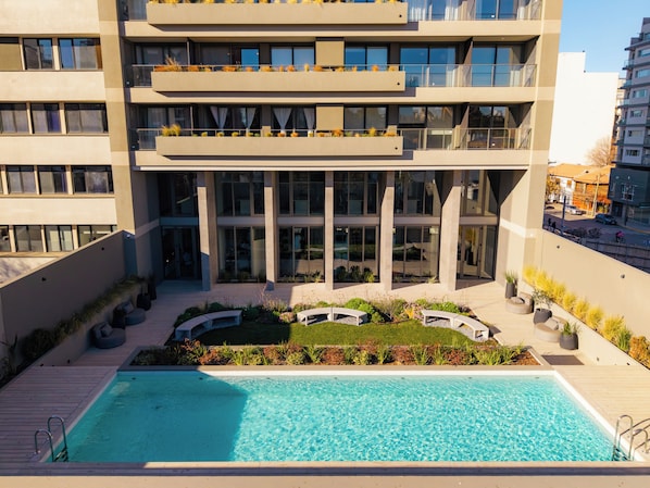 A modern building with a rooftop pool, outdoor seating, and a landscaped garden.