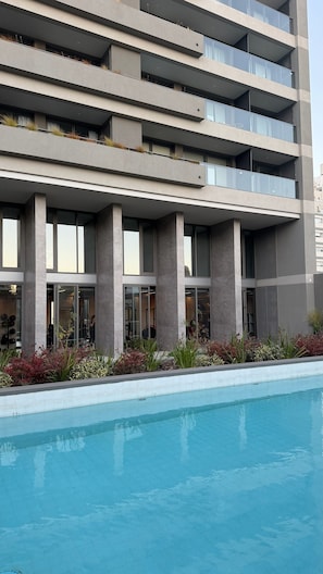 A modern building with a pool in front, featuring multiple balconies and large windows.