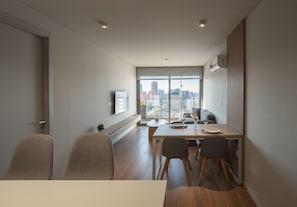 A modern dining area with a table set for four, a city view through large windows, and a ceiling-mounted air conditioning unit.