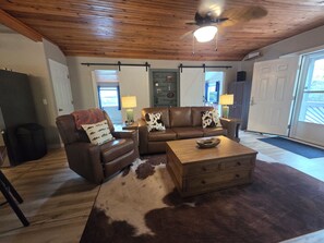 A living room with a brown leather sofa, a wooden coffee table, and a cowhide rug. - Rustic Riverfront Getaway — Close to Floating, Caverns, Golf & Route 66 (Cuba)