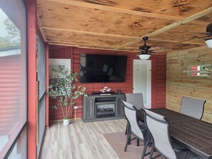 Une pièce avec un plafond en bois, un téléviseur à écran plat fixé au mur, une table à manger avec des chaises et une plante en pot.