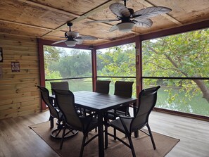 A dining area with a table and chairs, a ceiling fan, and a view of a river through large windows. - Rustic Riverfront Getaway — Close to Floating, Caverns, Golf & Route 66 (Cuba)