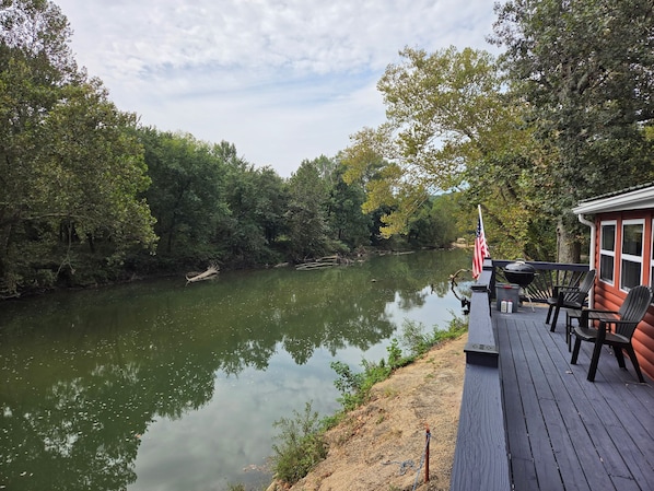 A deck with outdoor seating overlooking a calm river, surrounded by dense trees. - Rustic Riverfront Getaway — Close to Floating, Caverns, Golf & Route 66 (Cuba)