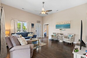 A spacious living room with a blue sofa, patterned armchairs, a coffee table, and a ceiling fan. - The Sea Turtle Hideaway𓇼Central+Cozy+Near Beach (Oak Island)