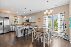 A modern kitchen with a central island, bar stools, and a dining table with chairs. - The Sea Turtle Hideaway𓇼Central+Cozy+Near Beach (Oak Island)